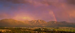 Enchanting aerial view capturing a rainbow's dance over Jocko Valley at sunset, framed by the mystical Mission Mountains